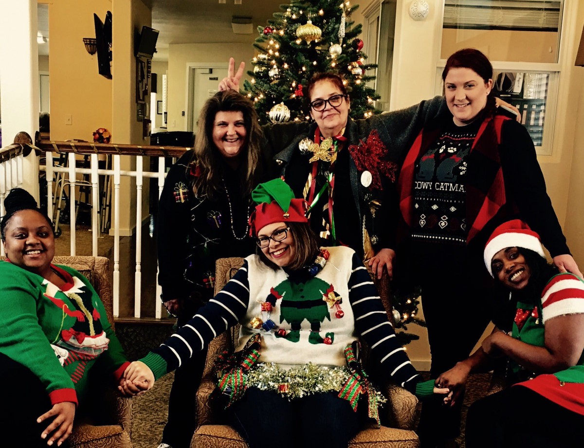 A group of people in festive clothing celebrating Christmas indoors near a decorated tree.
