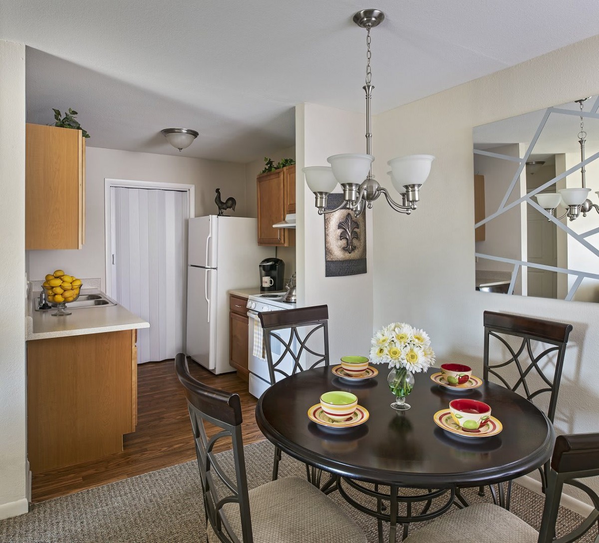 A cozy kitchen and dining area with a round table set for four, featuring a chandelier and decorative flowers.