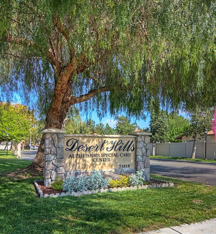 An entrance sign for Desert Hills Ranch Estates surrounded by lush greenery and trees.