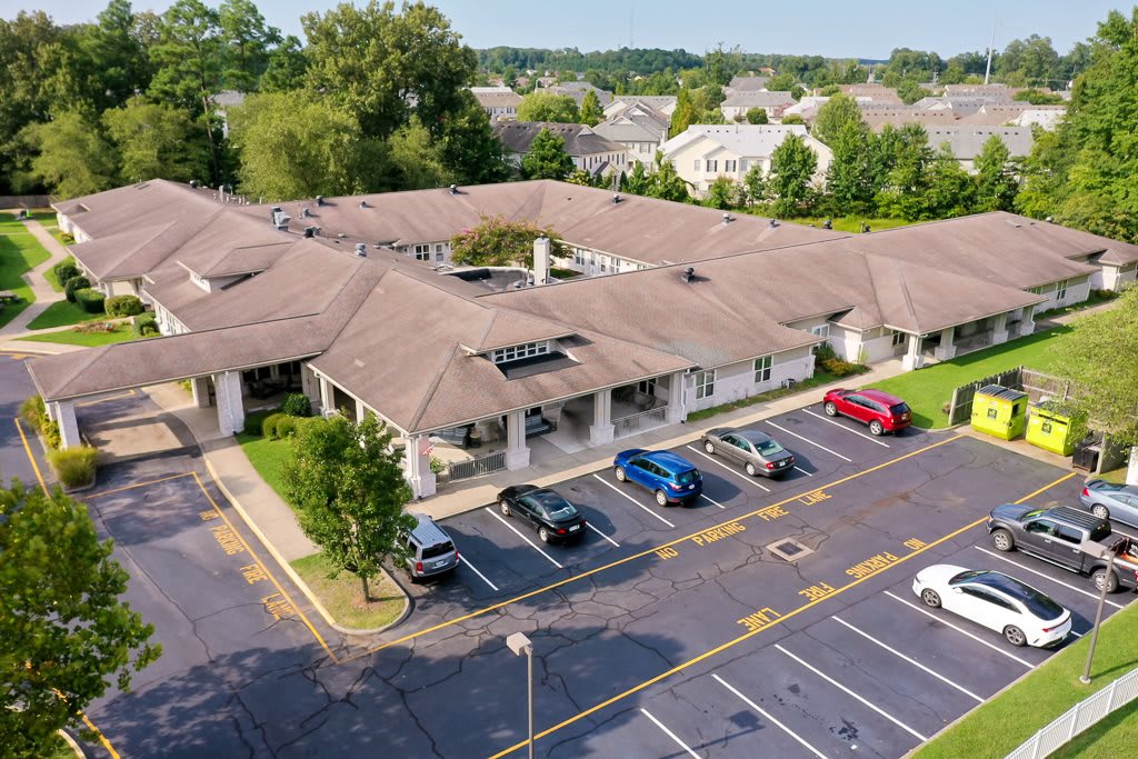 An aerial view of a building with a surrounding parking lot and cars, located in a residential area with trees.