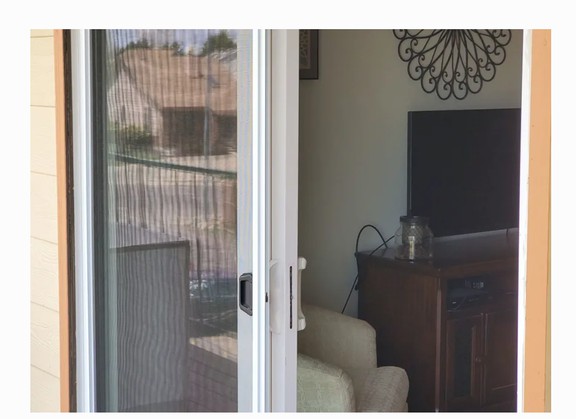 A sliding screen door opens to reveal a cozy living room with a television and furniture, with a balcony visible outside.