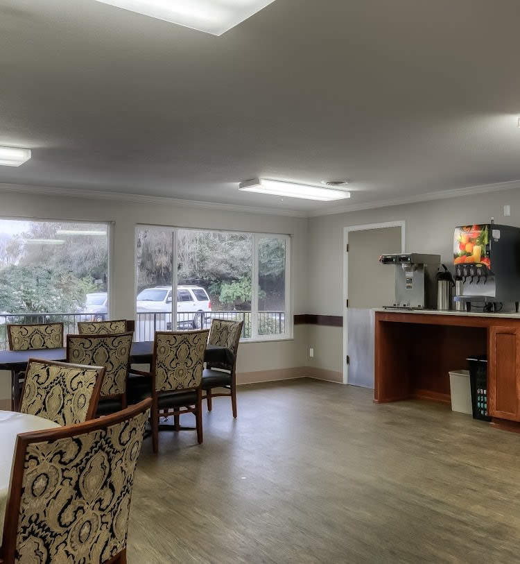 A spacious dining area with tables and chairs, featuring large windows and a coffee station.