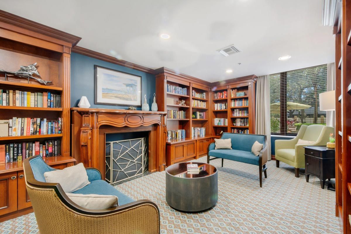 A cozy library with built-in bookshelves and a seating area surrounding a decorative fireplace.