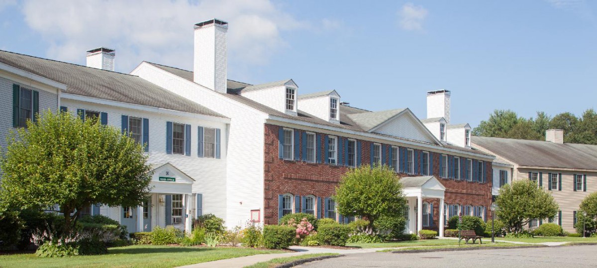 A suburban residential building with brick and white siding, surrounded by manicured landscaping.