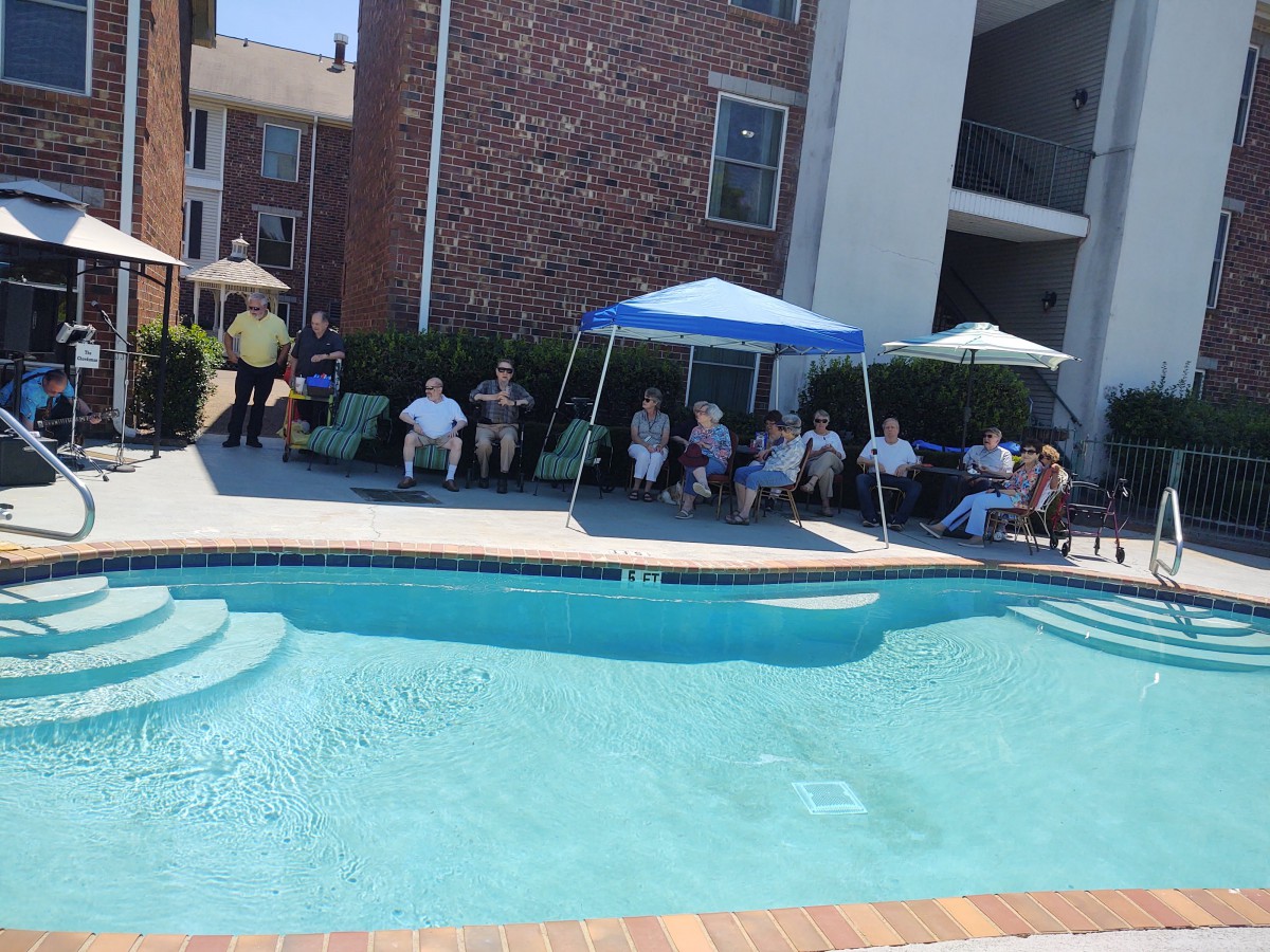 A group of people relaxing by the poolside under umbrellas at an apartment complex.