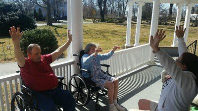 Elderly individuals enjoying a sunny day on the porch, sitting and raising their arms.