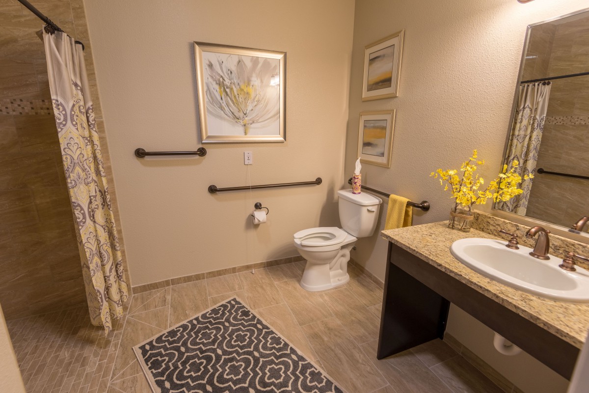An accessible bathroom with a toilet, sink, and grab bars, decorated with artwork and flowers.