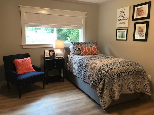 A cozy bedroom with a single bed, decorative pillows, and a bedside table topped with a lamp.