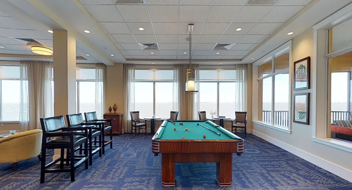 A spacious game room featuring a pool table with ample seating and large windows.