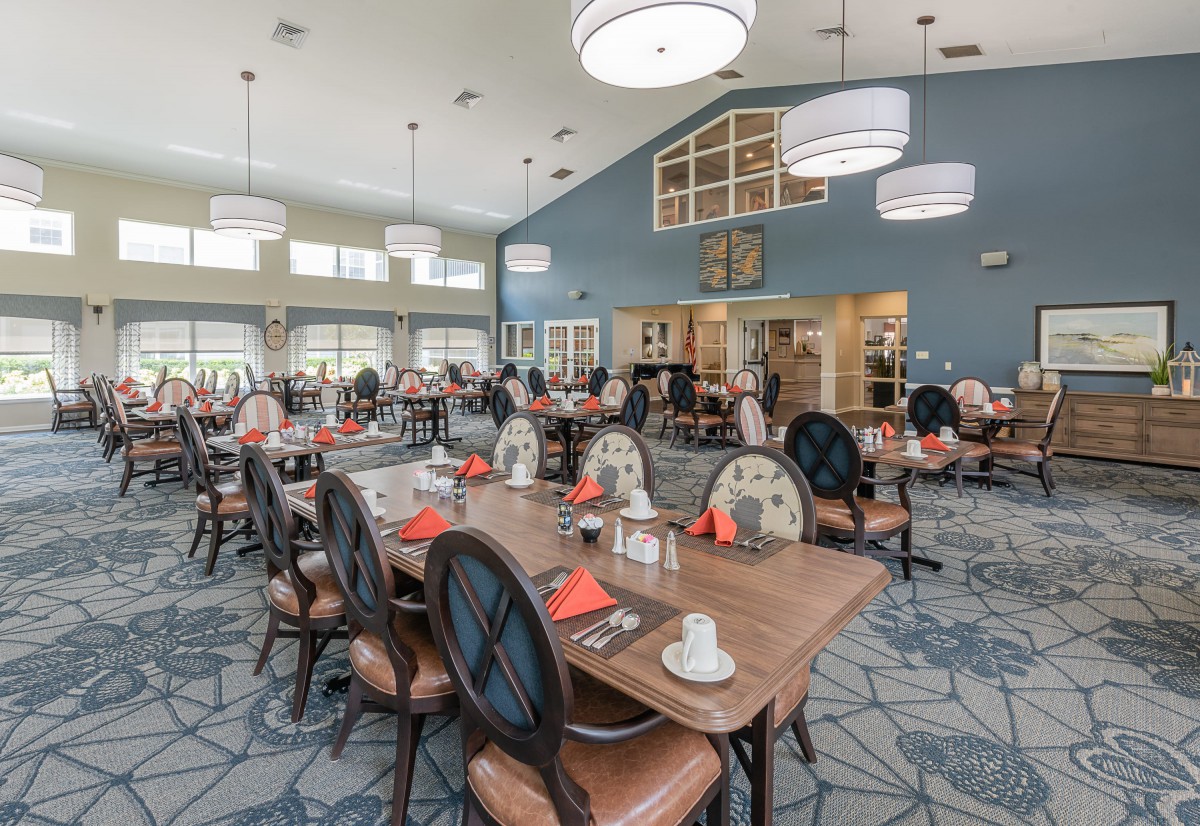 A spacious and elegantly designed dining room with multiple tables and chairs, featuring modern lighting fixtures.