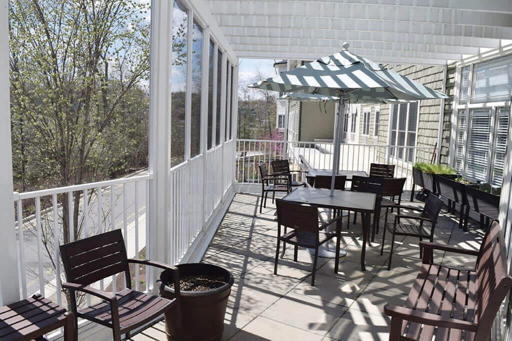 A sunny patio area with tables and chairs, partially shaded by a pergola.