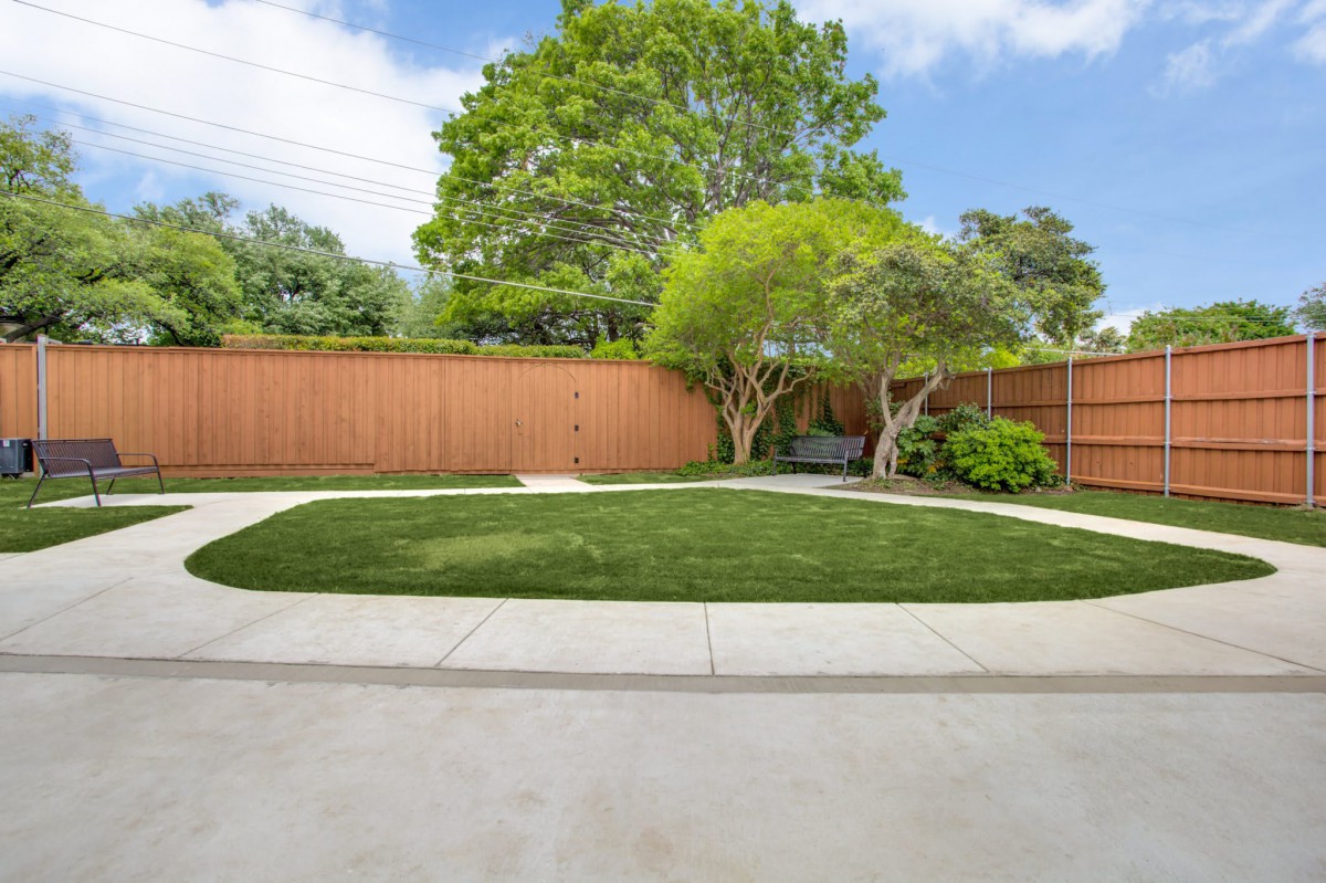 A well-maintained backyard with a lawn, trees, and a wooden fence.