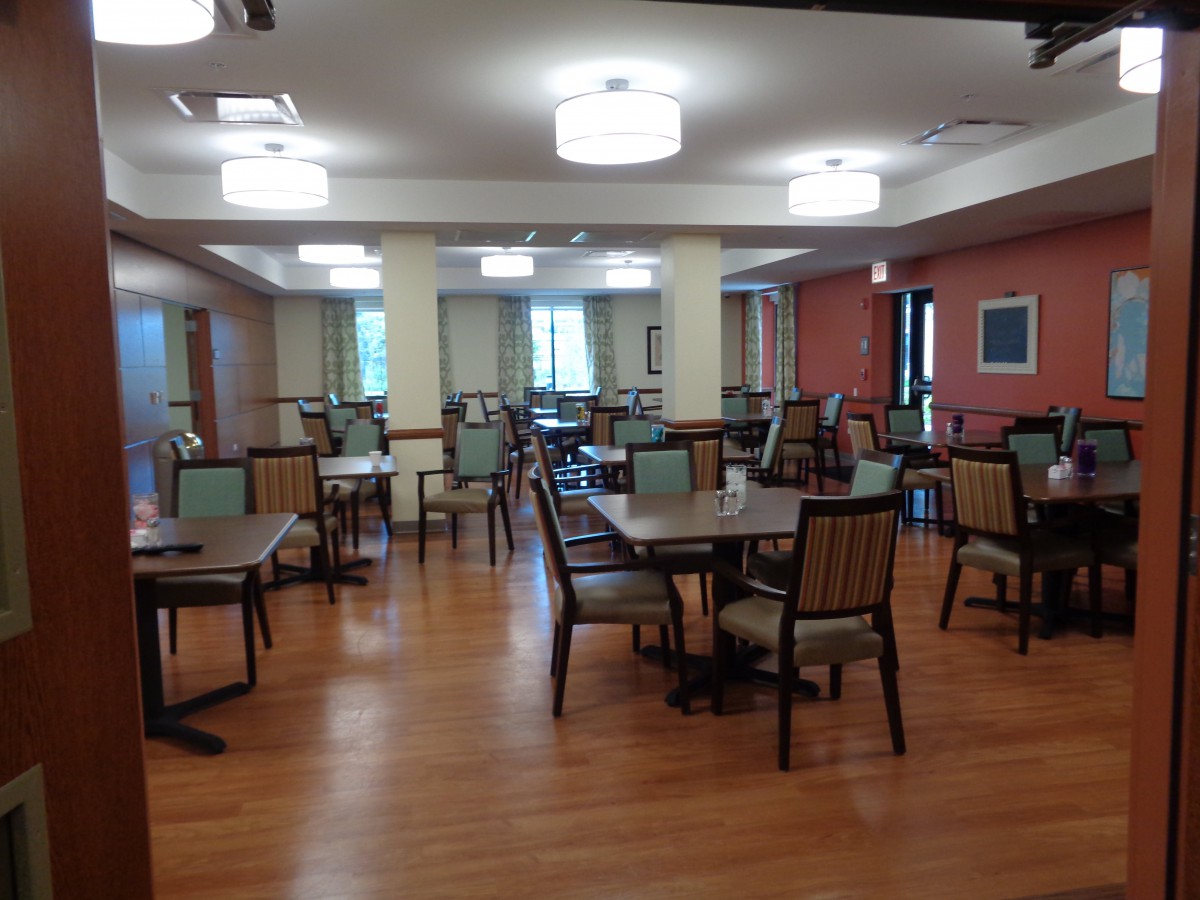 An empty dining room with neatly arranged tables and chairs, featuring a wooden floor and soft overhead lighting.