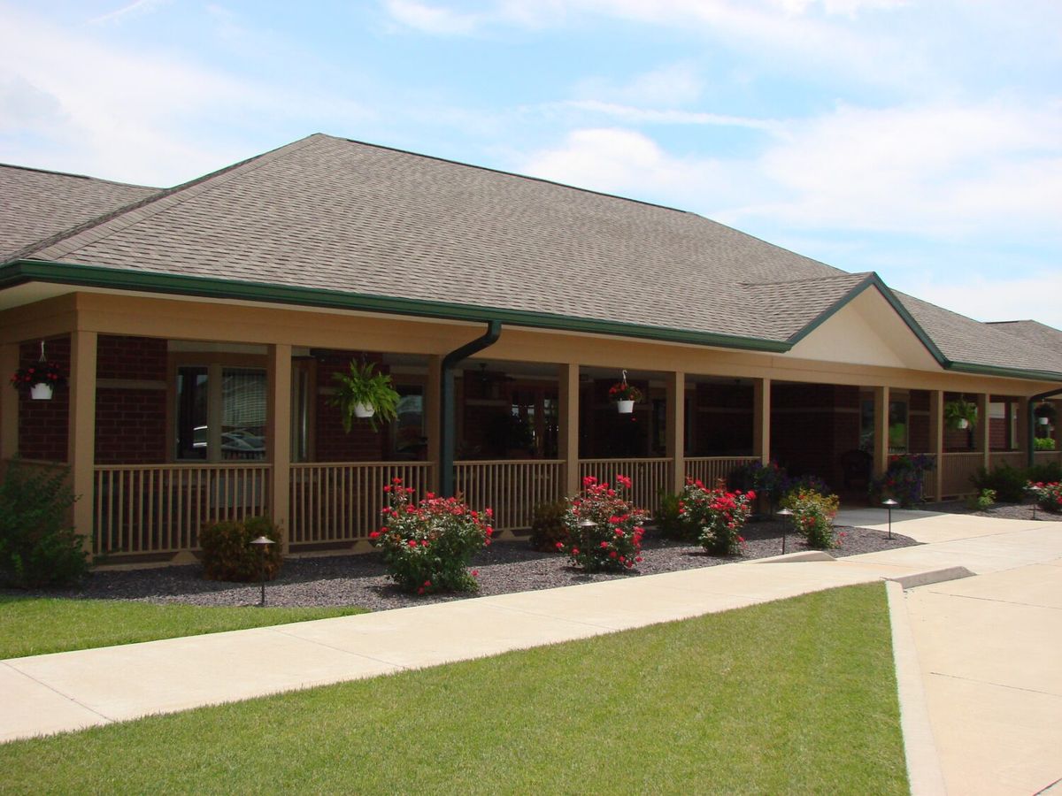 A residential building with a spacious porch, surrounded by a well-maintained garden and lawn.