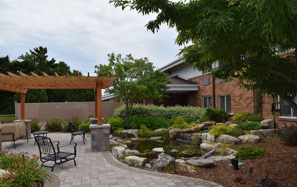A beautifully landscaped garden featuring a stone pathway, pergola, pond, and seating area.