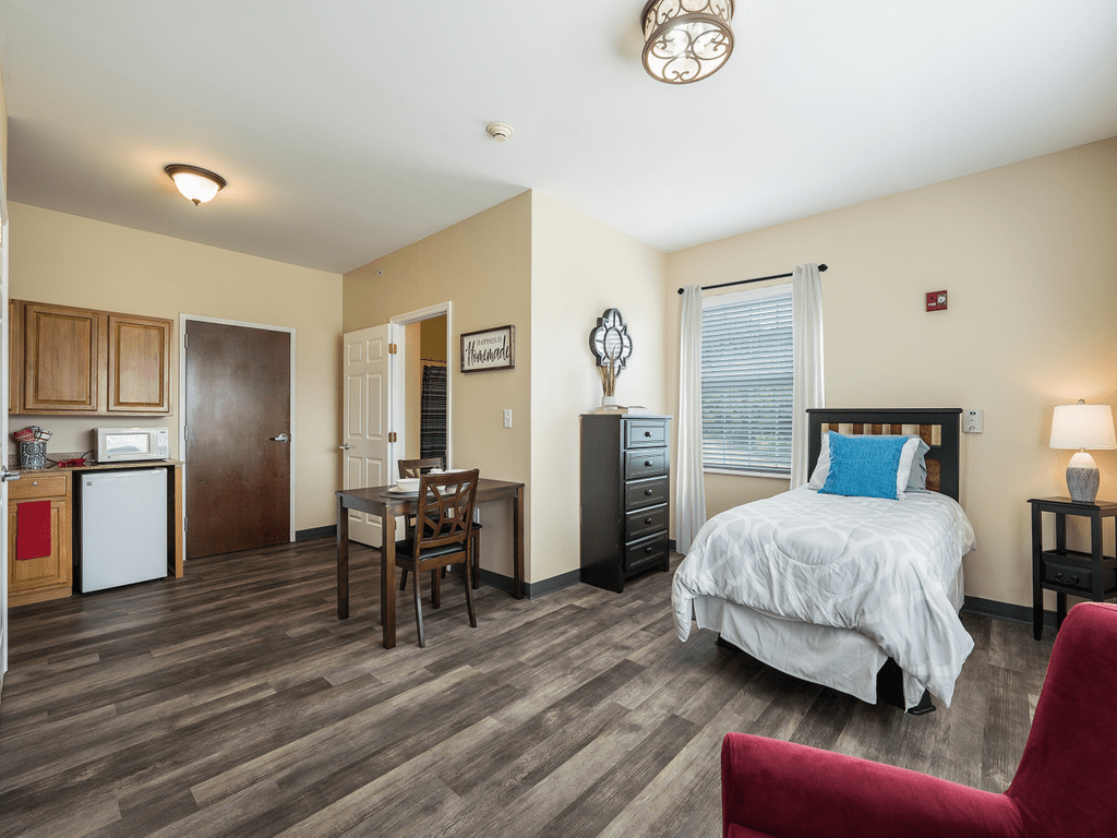 A cozy bedroom with a single bed, wooden flooring, and natural light streaming through the window.