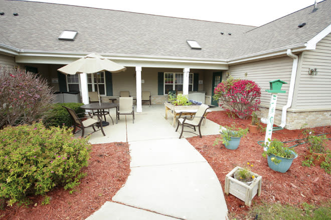 A cozy outdoor patio with seating, tables, and surrounding landscaping.