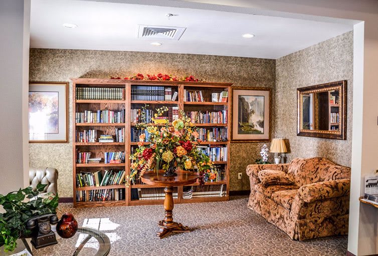 A cozy reading room with a large bookshelf, floral arrangement, and comfortable seating.