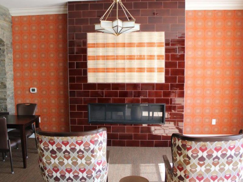 A cozy living room featuring a tiled fireplace with patterned chairs and orange wallpaper.