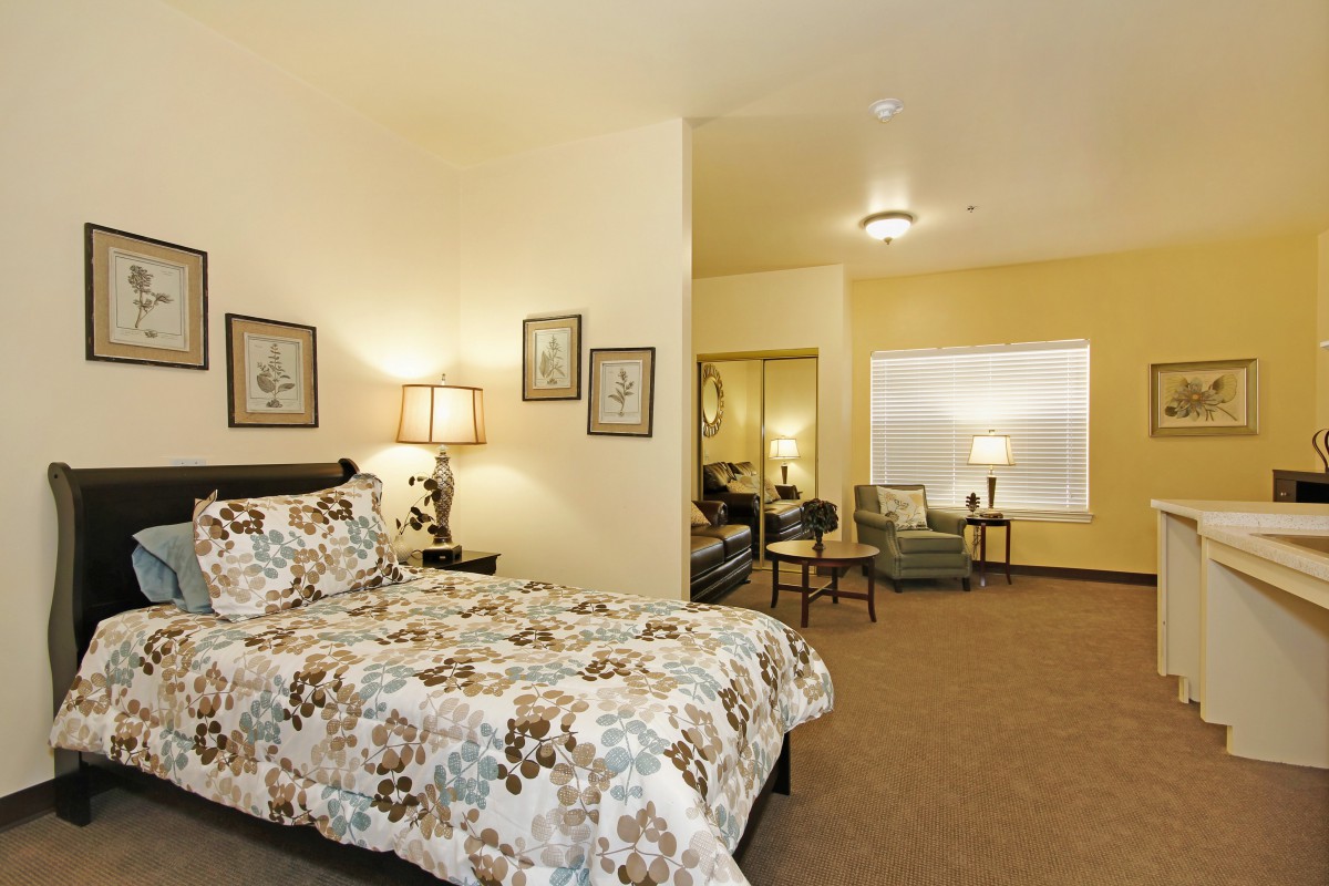 A cozy bedroom interior featuring a bed with floral bedding, a seating area, and warm lighting.
