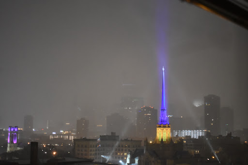 A misty night view of a city skyline illuminated by colorful lights amidst rain.