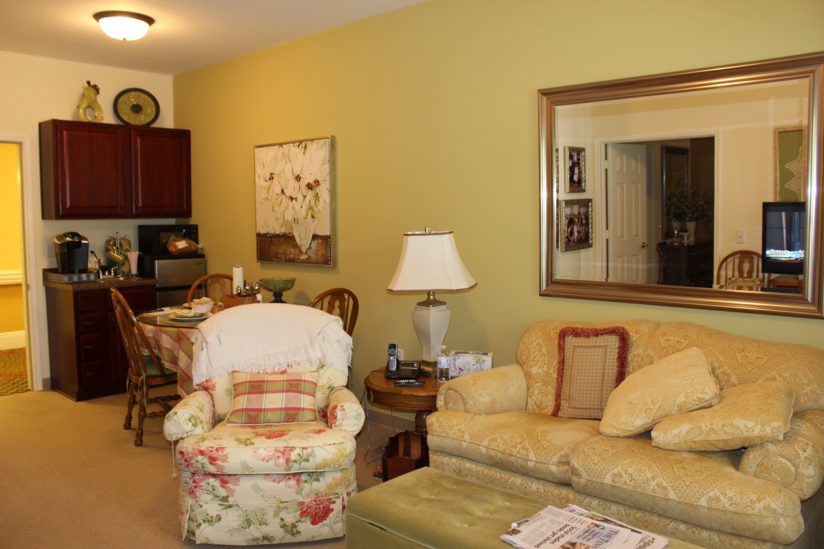 A cozy living room with a floral armchair, yellow sofa, and various decorative elements.