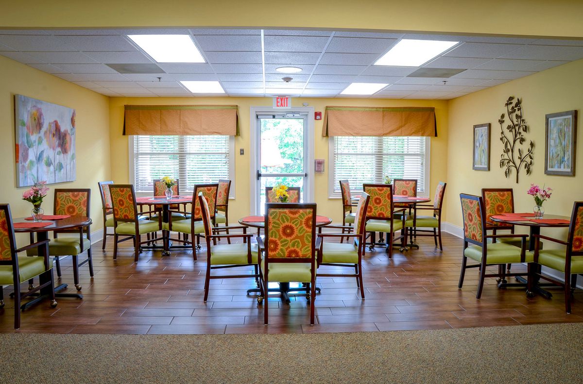 A cozy dining room with multiple tables and chairs, featuring bright lighting and wooden flooring.