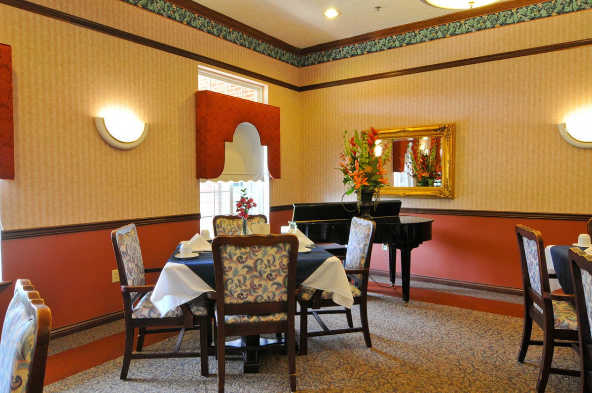 A cozy dining area with a table set for four, decorated with flowers and featuring a grand piano.