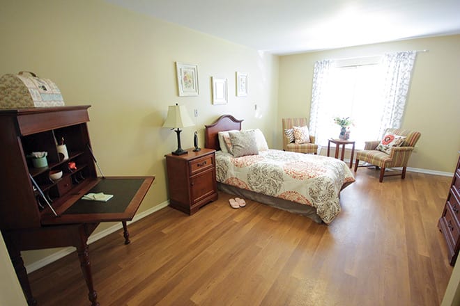 A cozy bedroom with a single bed, desk, and a large window letting in natural light.
