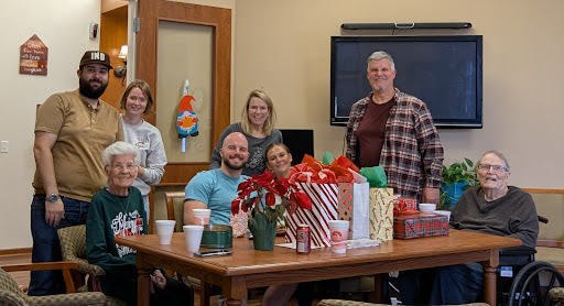 A cheerful group of friends enjoying a festive Christmas gathering surrounded by presents and holiday decorations.