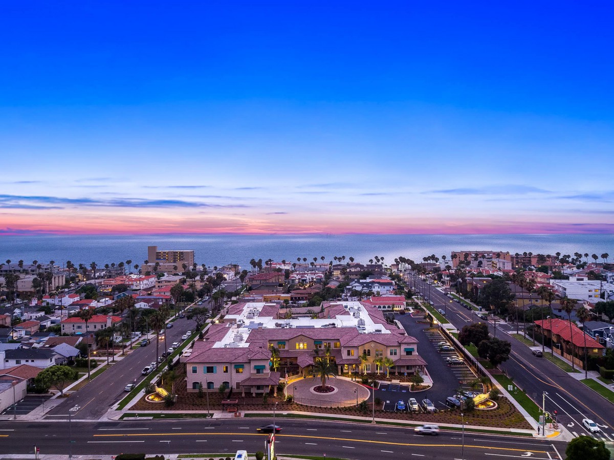 Aerial view of a coastal cityscape at sunset, featuring buildings and roads leading to the ocean.