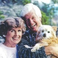 An elderly couple smiling while holding their dog outside.
