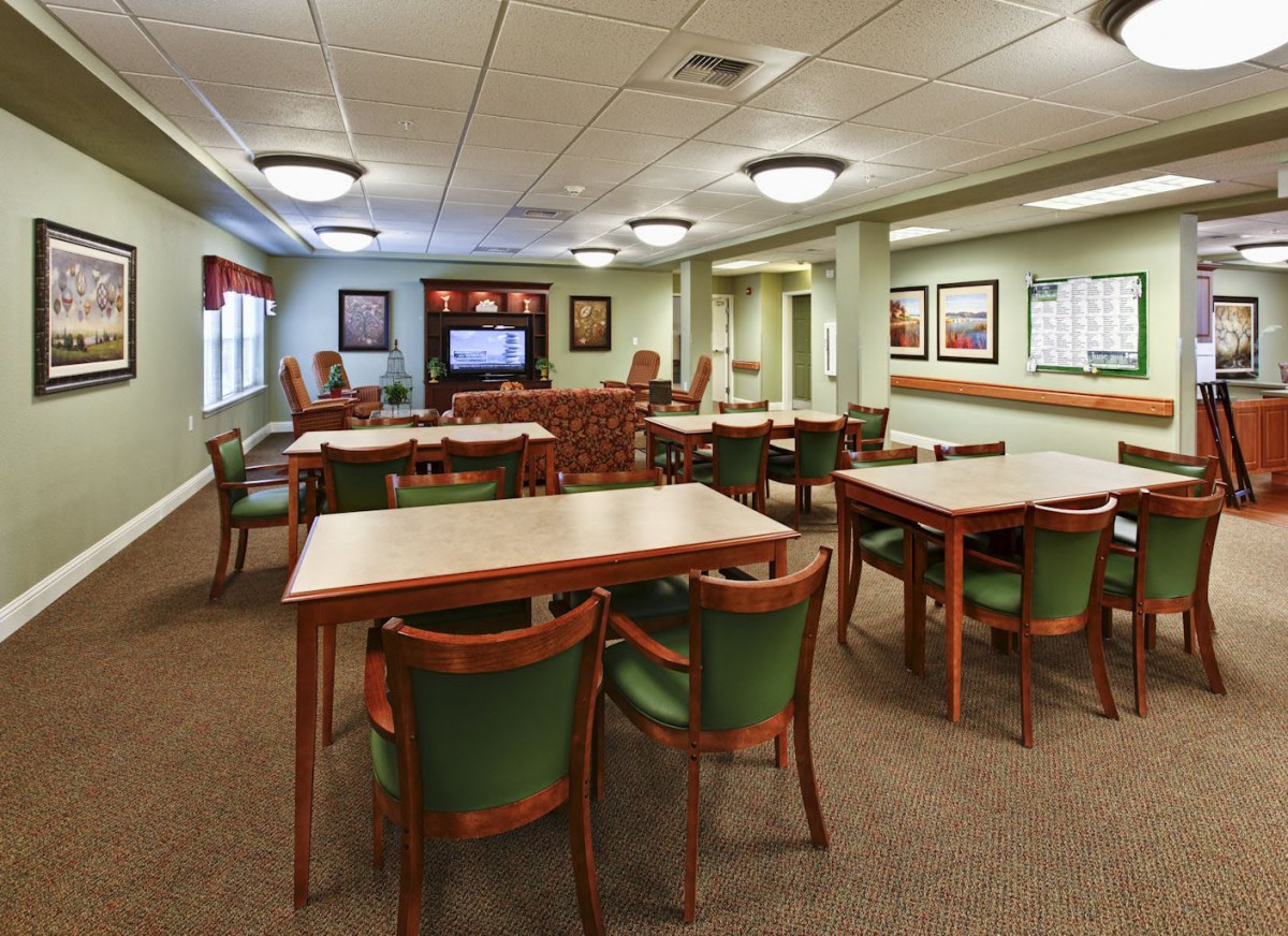 A well-lit meeting room with multiple tables and chairs, featuring a television and wall decor.