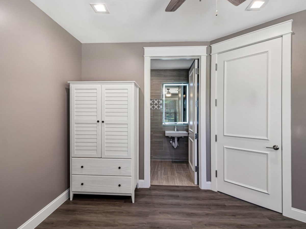 A modern bedroom features a white wardrobe and leads into an attached bathroom with wood flooring and neutral tones.
