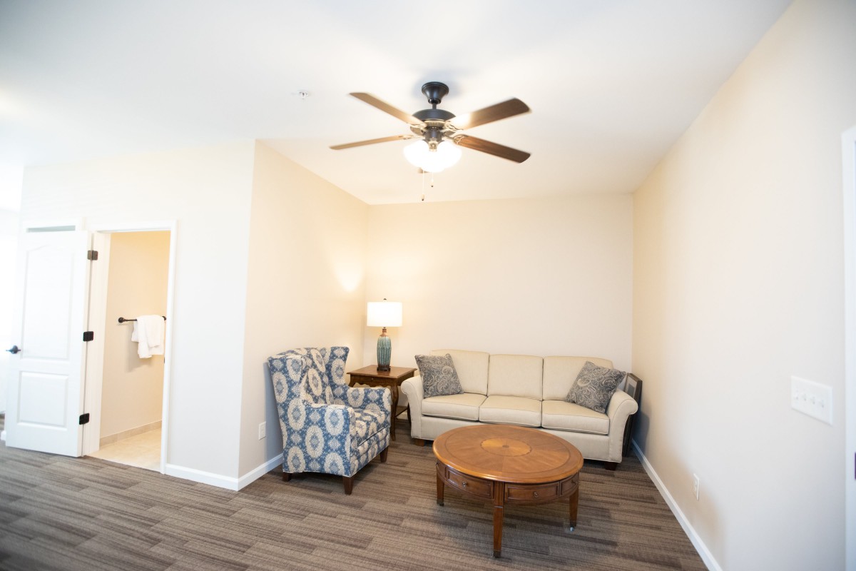 A cozy living room with a couch, armchair, and coffee table under a ceiling fan.