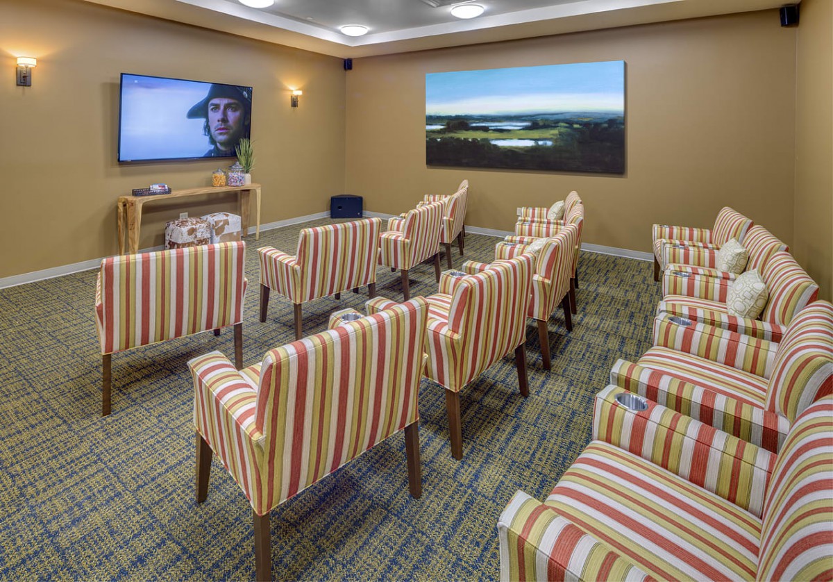 A cozy home theater room with striped chairs arranged in rows facing a large television screen.