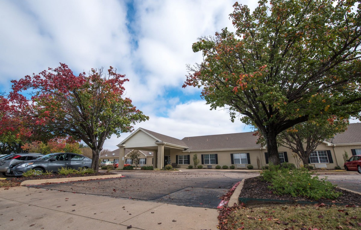 A suburban building with a parking lot and surrounding trees under a cloudy sky.