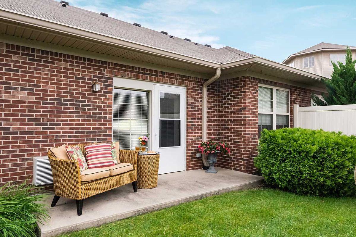 A cozy patio with outdoor seating against a brick house, surrounded by a well-maintained lawn.