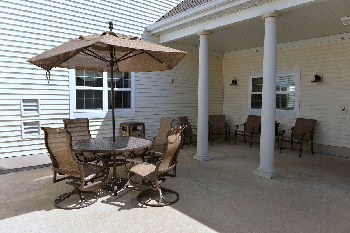A cozy outdoor patio area with a table, chairs, and an umbrella under a covered space.