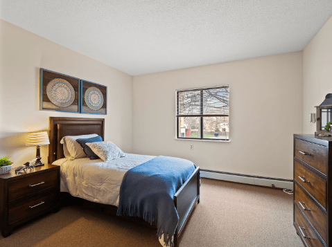 A cozy bedroom with a single bed and wall art, featuring a window allowing natural light to flood in.