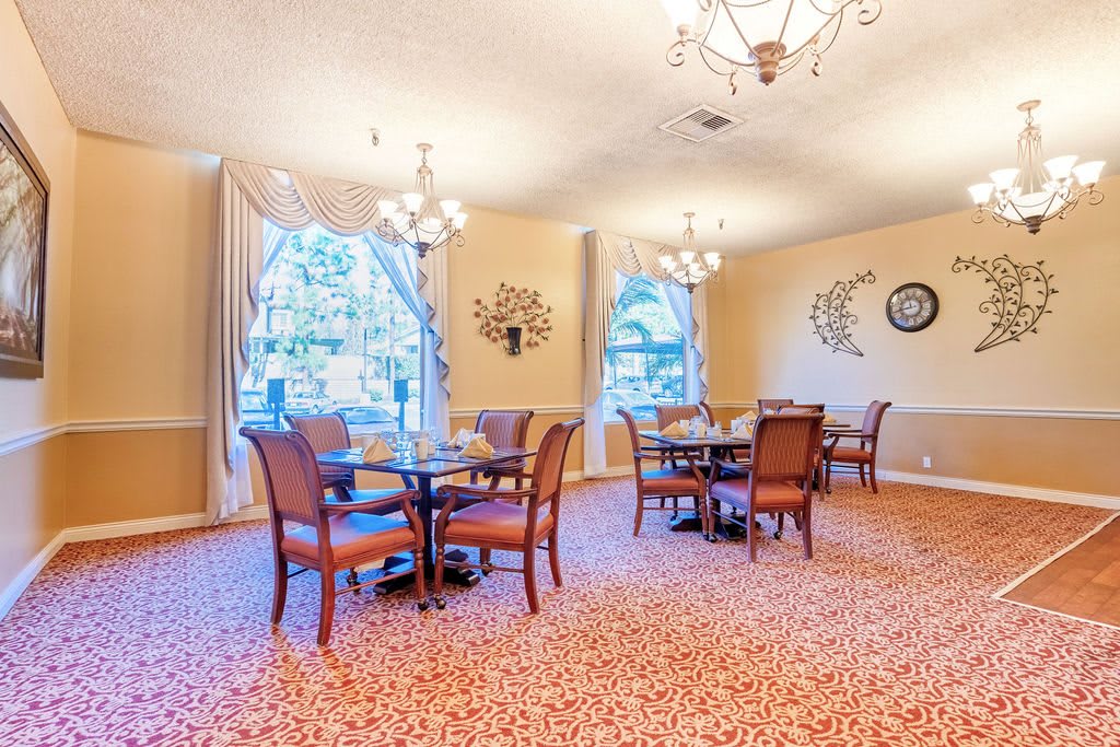 A cozy dining room with elegant chandeliers, neatly arranged tables, and upholstered chairs.