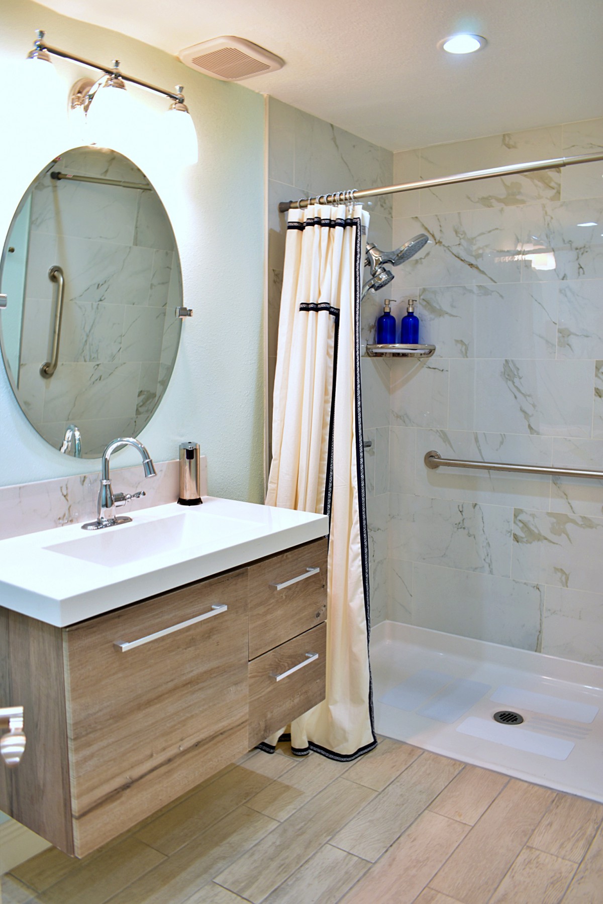 A modern bathroom with a vanity, shower, and oval mirror.