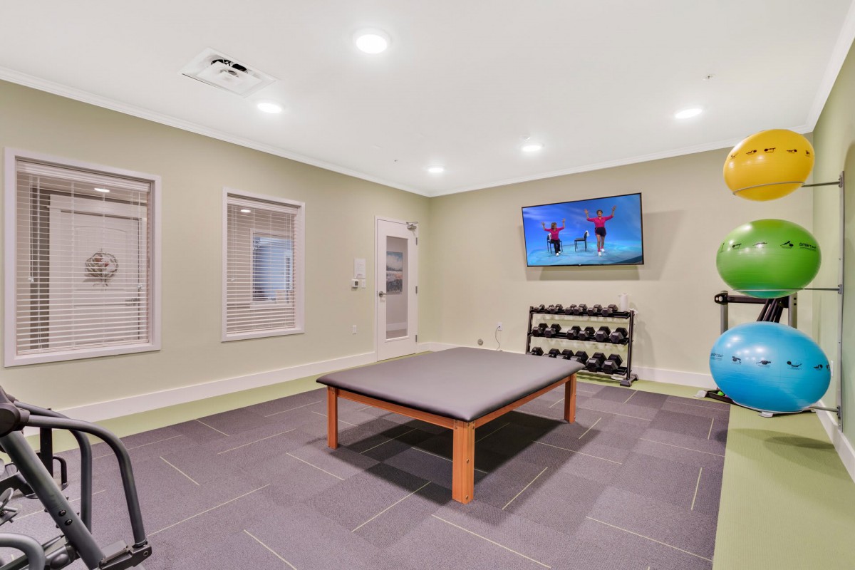 A modern home gym with a mounted television, dumbbells on a rack, and ample space for exercise.