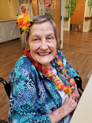A joyful elderly woman dressed in colorful attire, adorned with flowers, enjoying a cheerful moment.