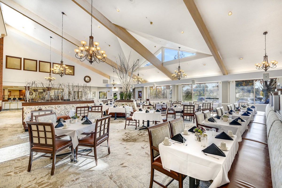 An elegant restaurant dining area with chandeliers, white tablecloths, and neatly arranged tables and chairs.