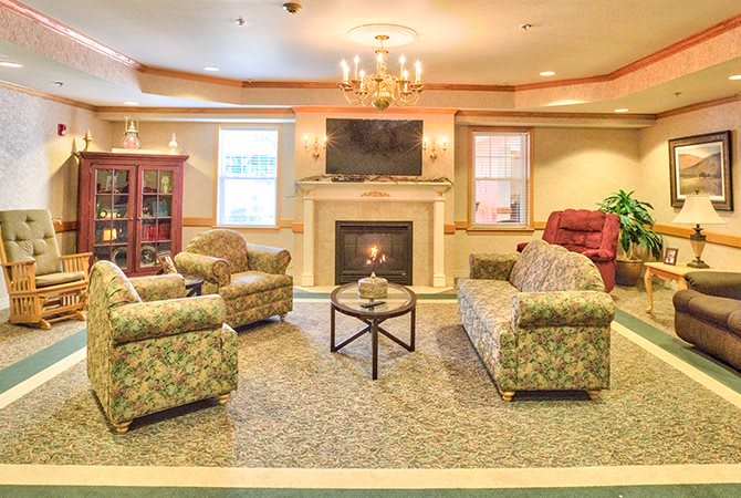 A cozy living room featuring a fireplace, sofas, and armchairs arranged around a central table, with a television mounted above the fireplace.