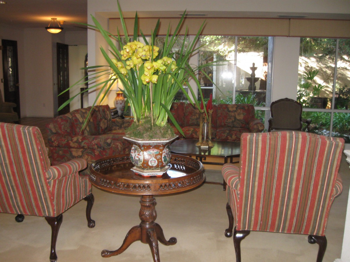 A cozy living room featuring a central table with a floral arrangement, surrounded by upholstered chairs and a sofa.