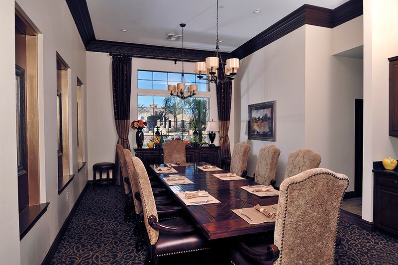 An elegant dining room with a large table, high-backed chairs, and a chandelier, featuring a window view.