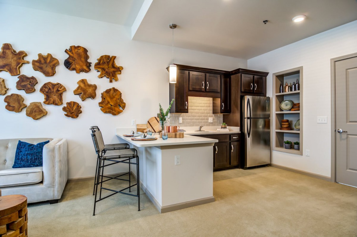 A modern kitchen interior with dark wood cabinets, stainless steel appliances, and bar seating.