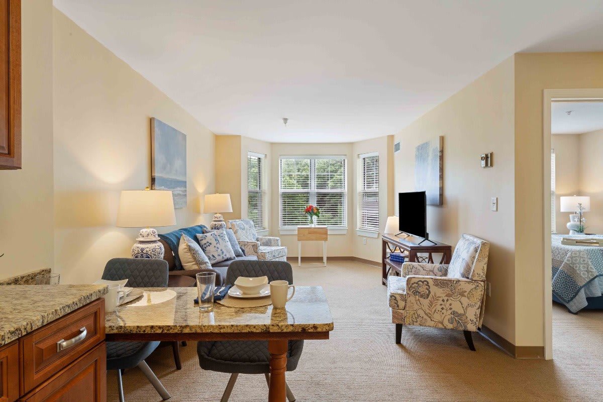 A bright and cozy living room with a dining area, featuring comfortable seating and large windows.